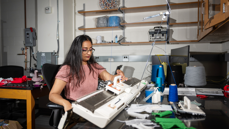 A female student operating a knitting machine in a research lab at Georgia Tech.